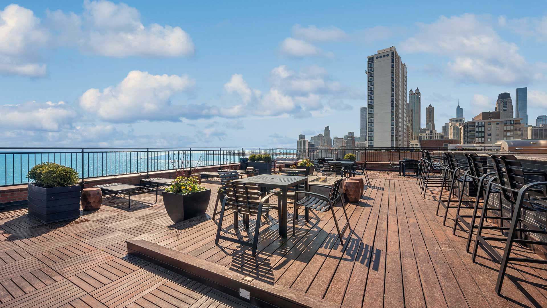 Looking across the rooftop deck with Lake Michigan and the Chicago skyline in the background. Various deck furniture is set throughout the deck.